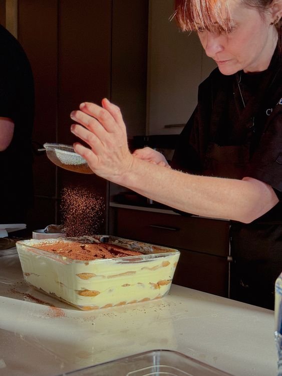 Mani che spolverano cacao amaro su un tiramisù