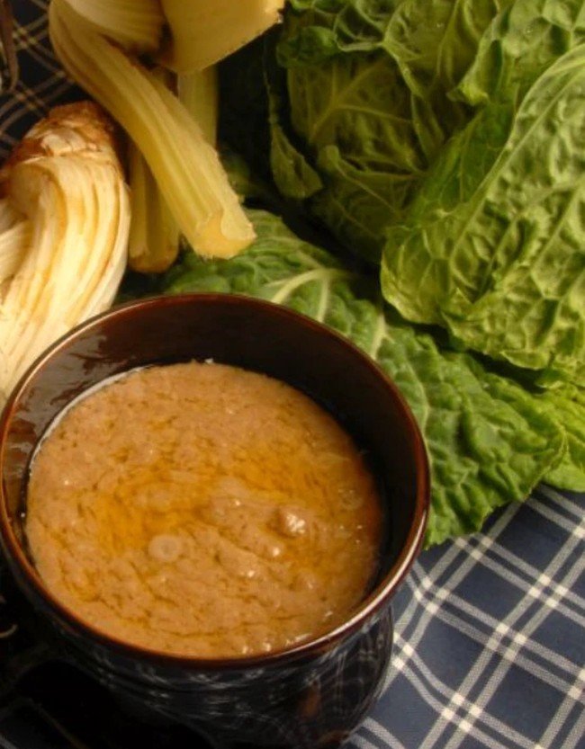 Ciotola di bagna cauda accanto a cardi, verza e finocchio
