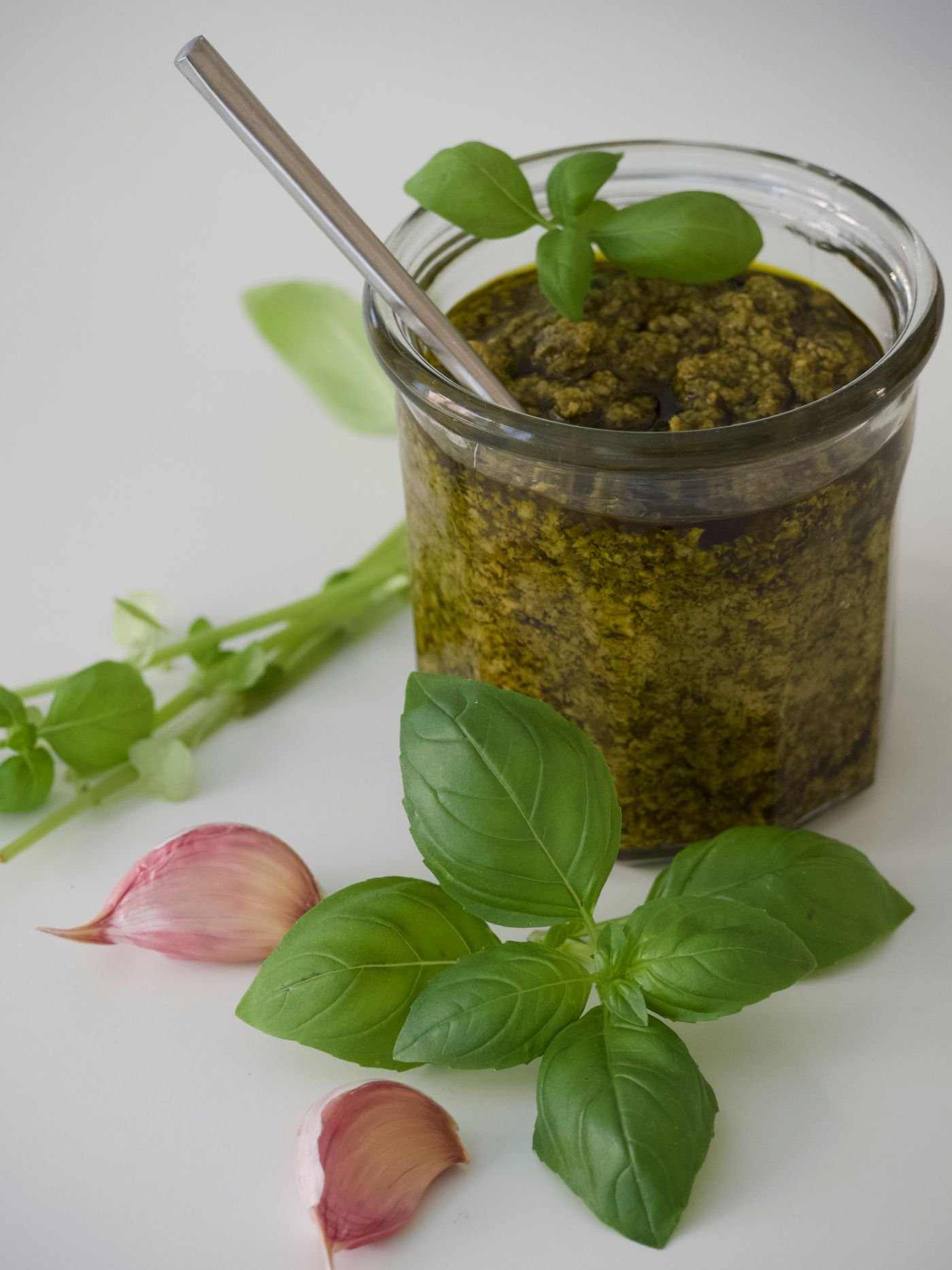 Vasetto di vetro con pesto, foglie di basilico e spicchi d'aglio accanto