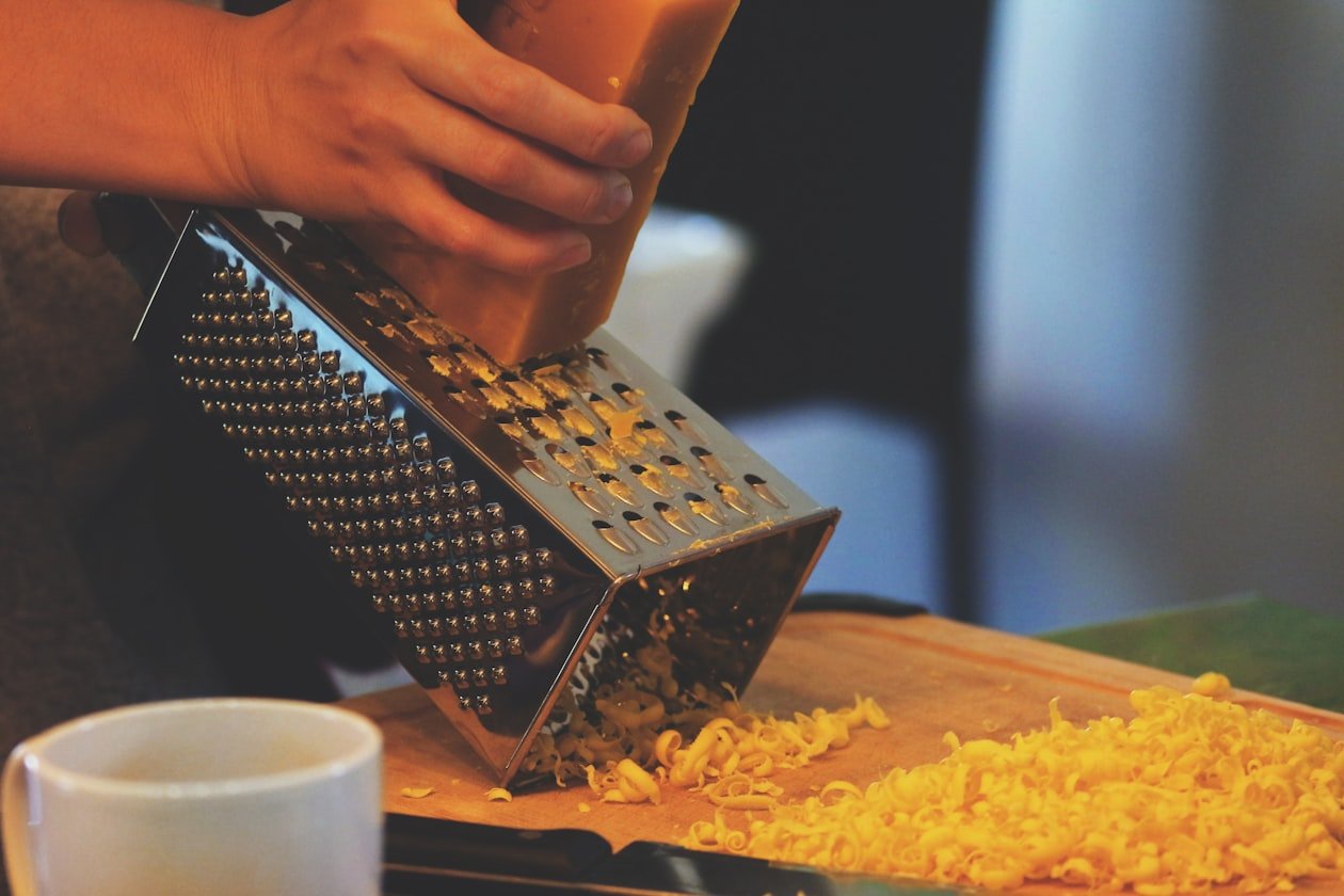 Mano che gratta il formaggio sul tagliere