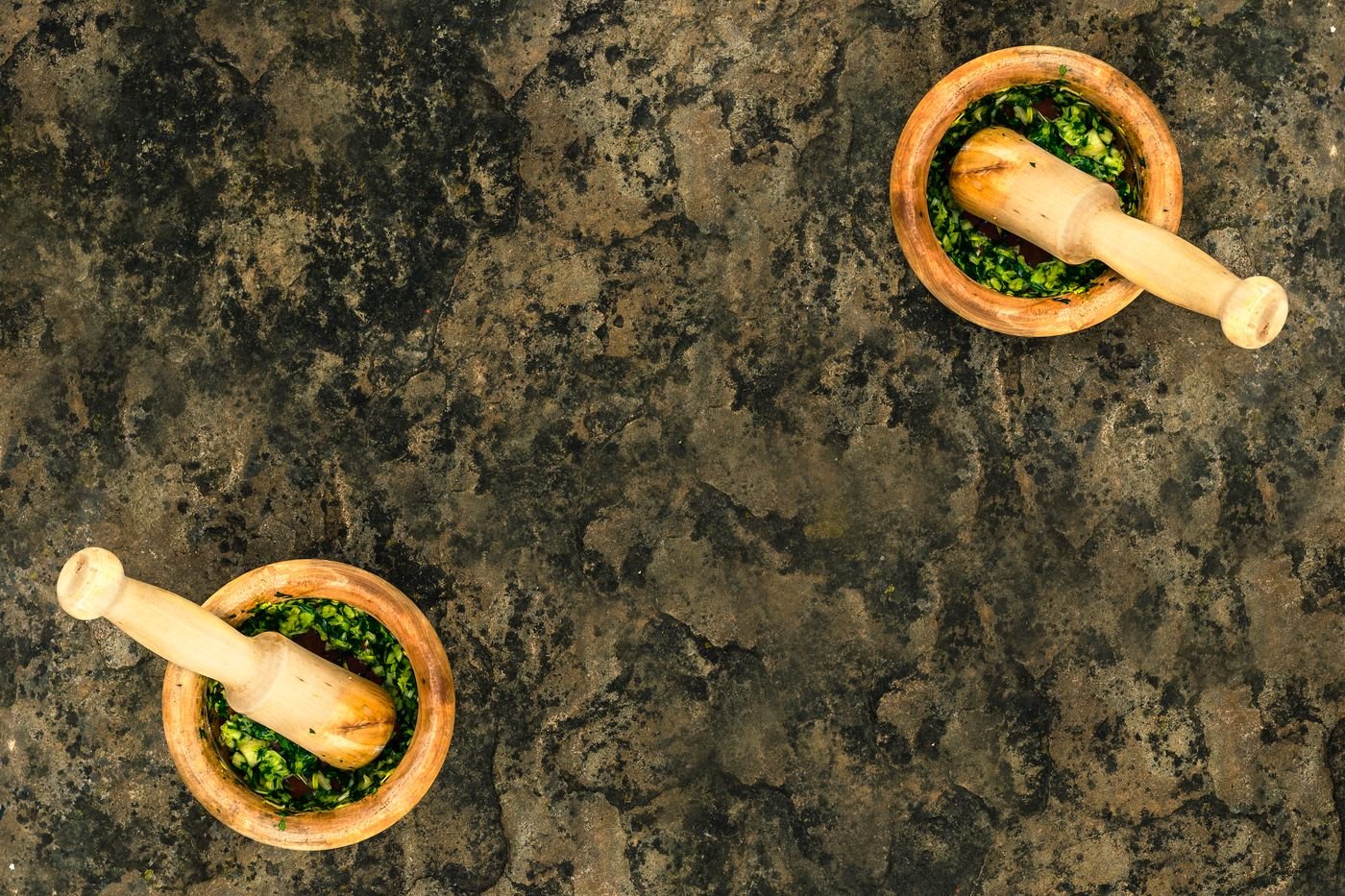 Due mortai di legno con dentro il pesto appena fatto, su un piano di pietra