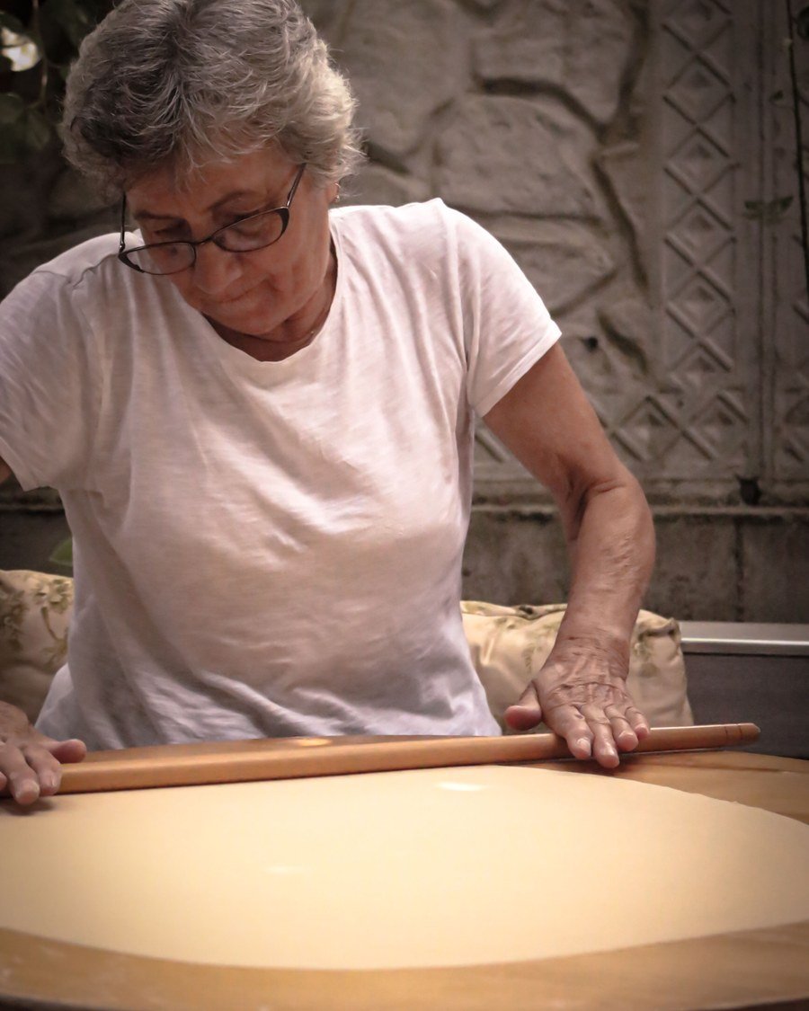 Sfoglina che tira la sfoglia col matterello sul tagliere tondo