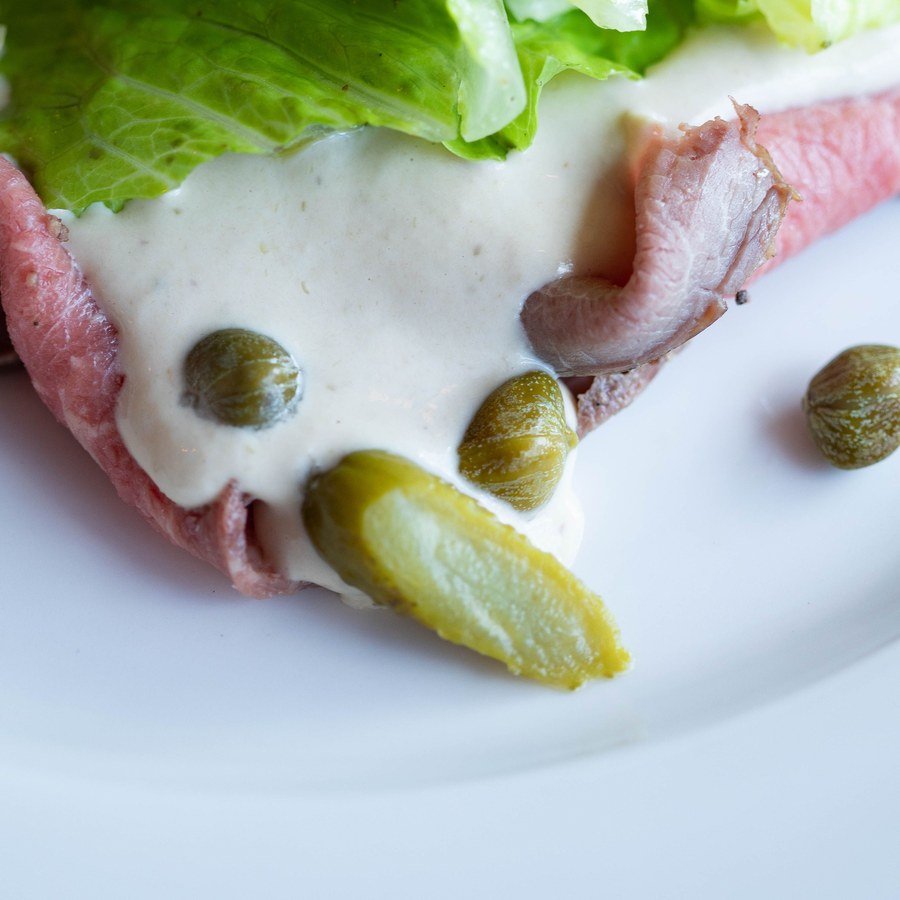 Fetta di vitello coperta dalla salsa tonnata, con capperi e cetriolino